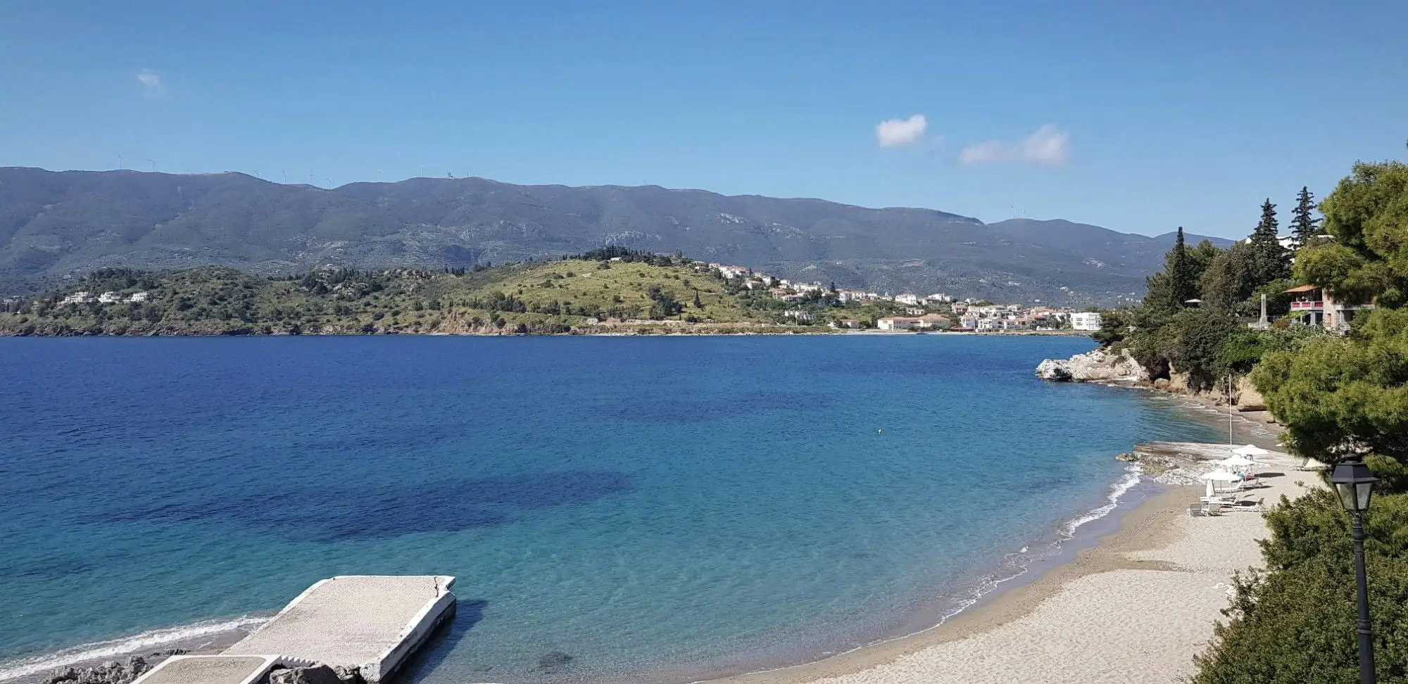 A curving sandy beach on Poros, with wooded hills across the water